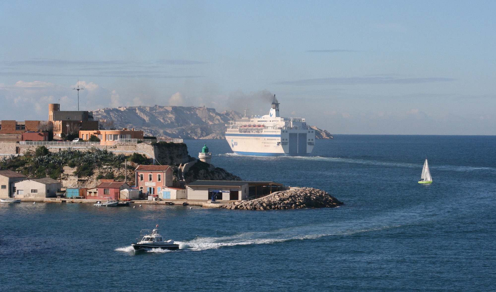 Eine große weiße Fähre verlässt den Hafen von Marseille und passiert die vorgelagerte Felsküste